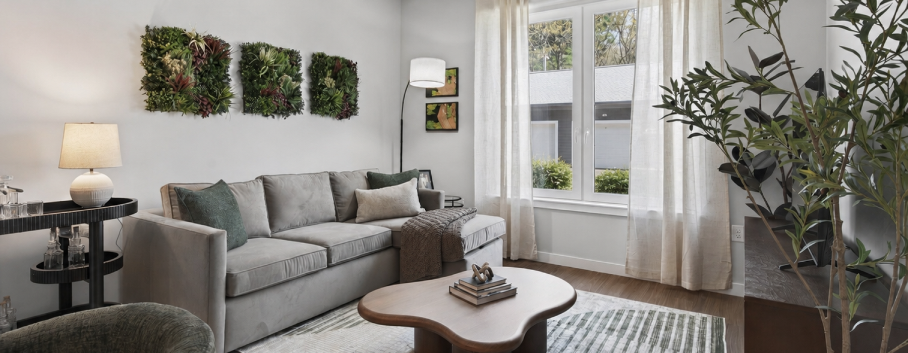 Model apartment with grey couch, brown coffee table, a bar cart with glasses, and view of garage outside 