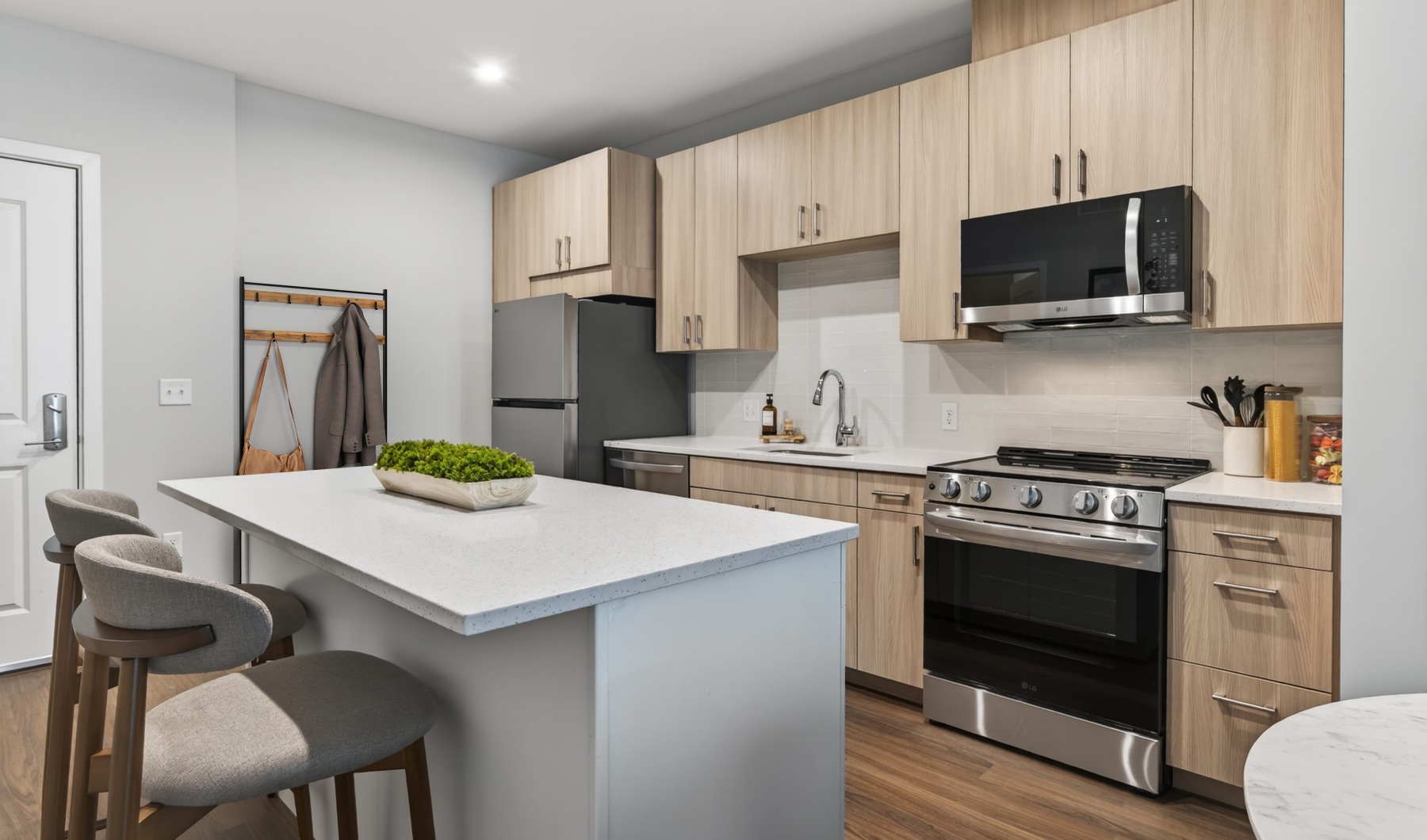 Furnished kitchen with island barstool seating, natural kitchen cabinets, white quartz countertops and stainless steel appliances